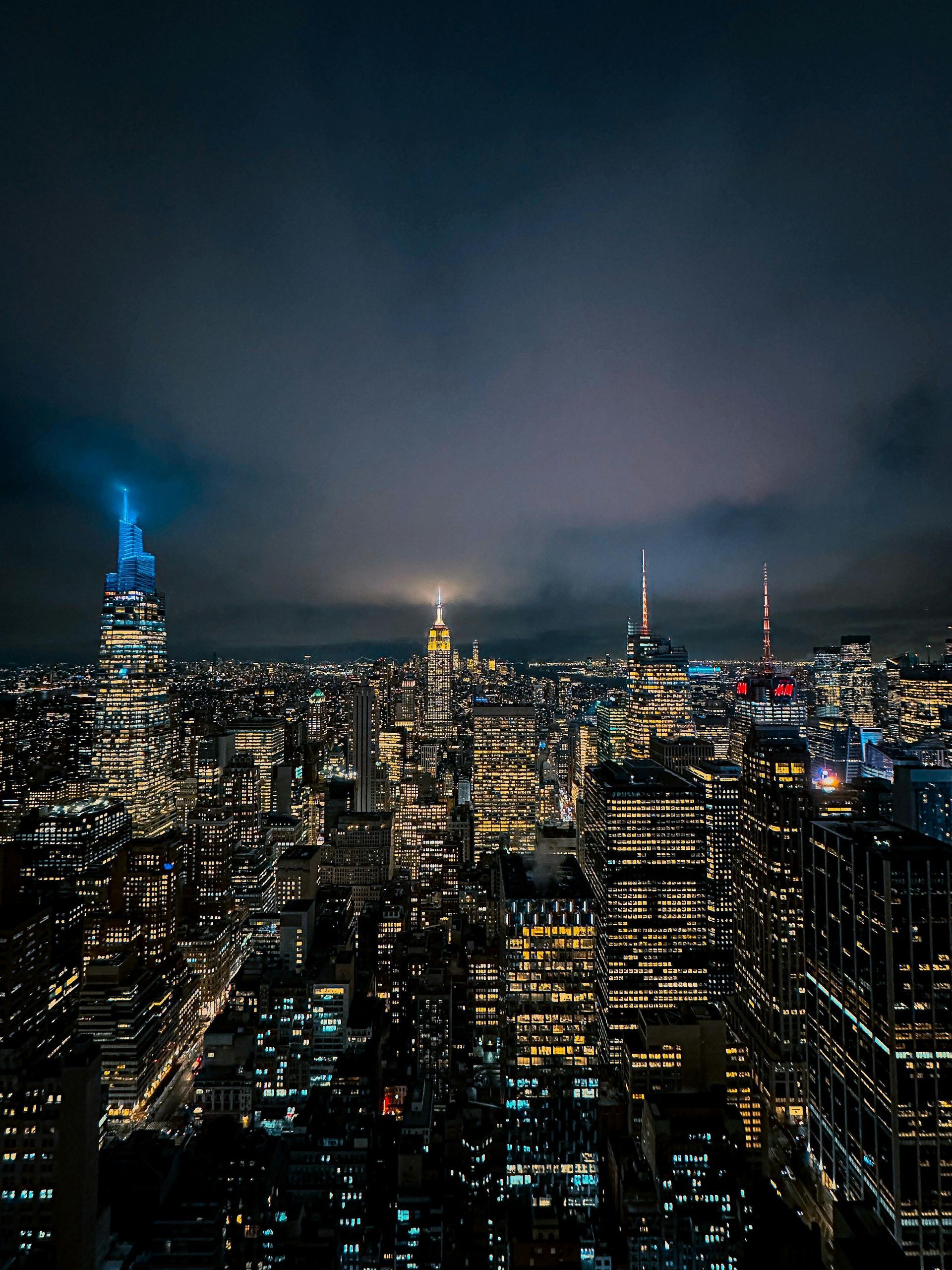 City skyline at night, illuminated skyscrapers under a cloudy sky.