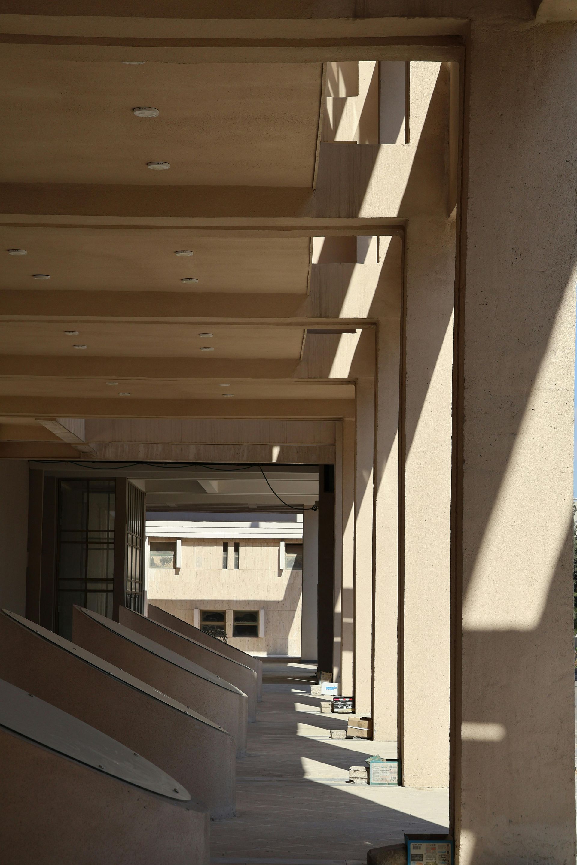 Building exterior with a covered walkway and shadows cast by pillars. Light tan color.