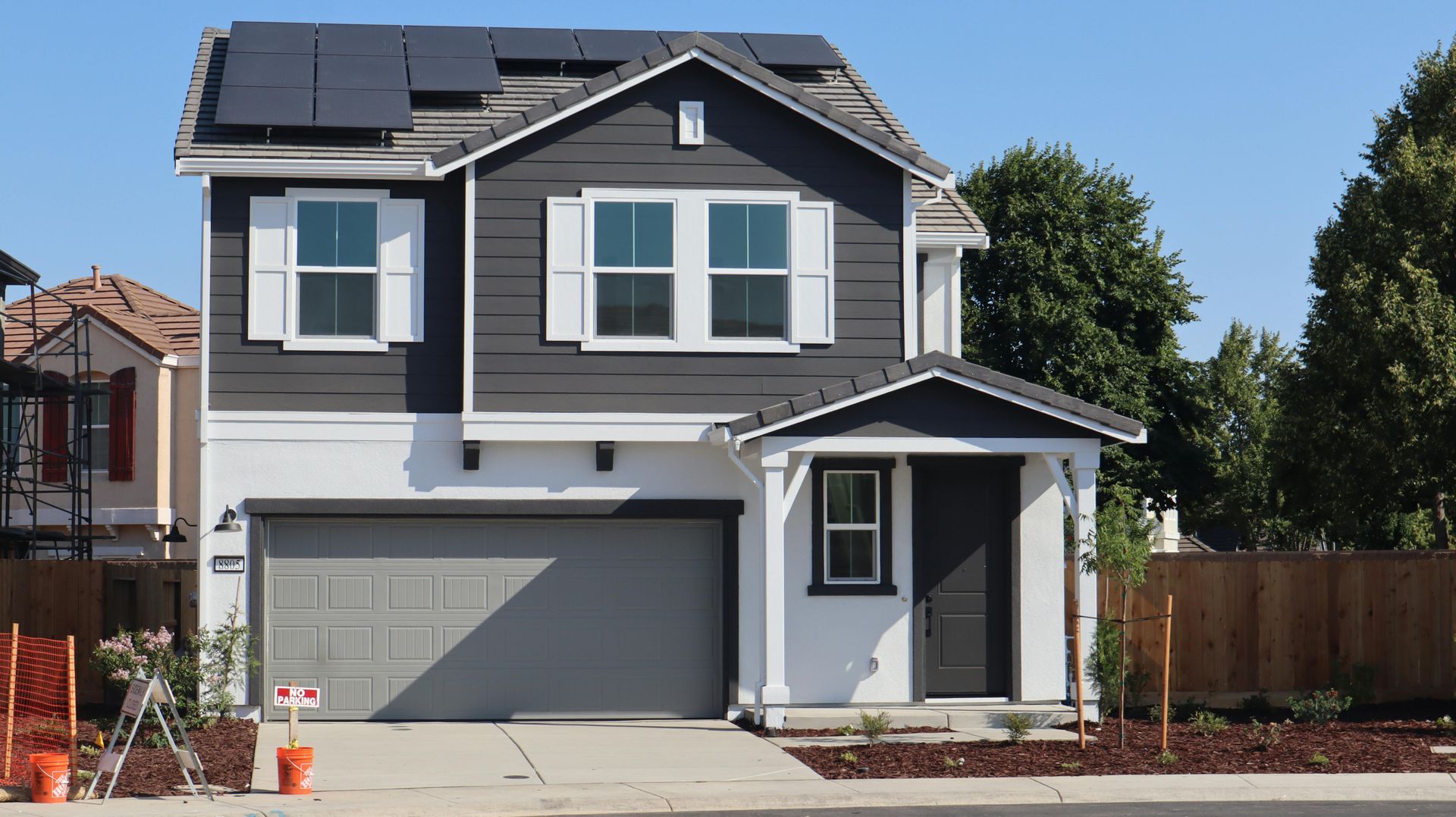 Two-story house with dark gray siding, white trim, gray garage, and solar panels on the roof.
