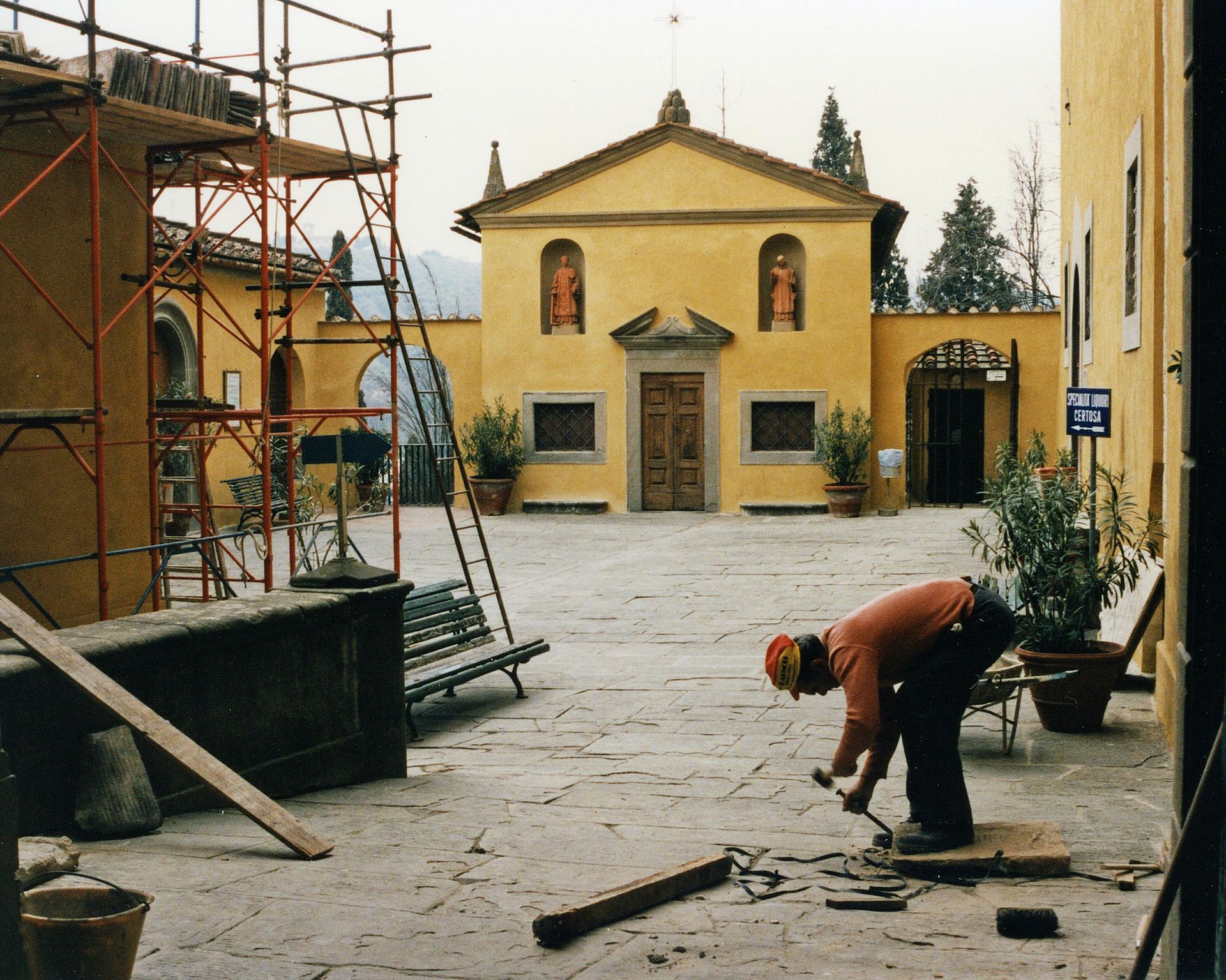 Man working on stone in courtyard with yellow building in background.