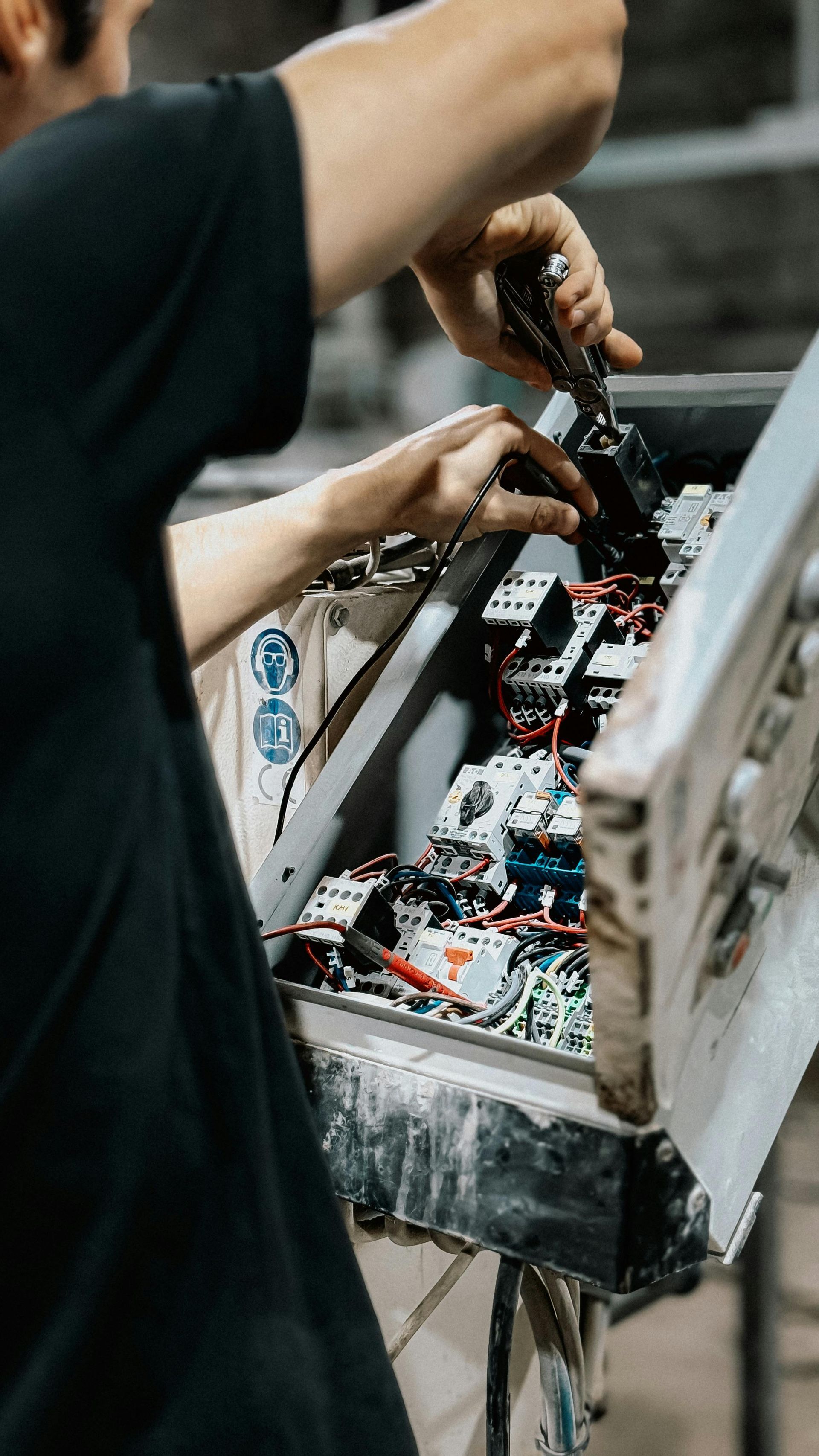 Person using tools to work on electrical components inside a metal enclosure.