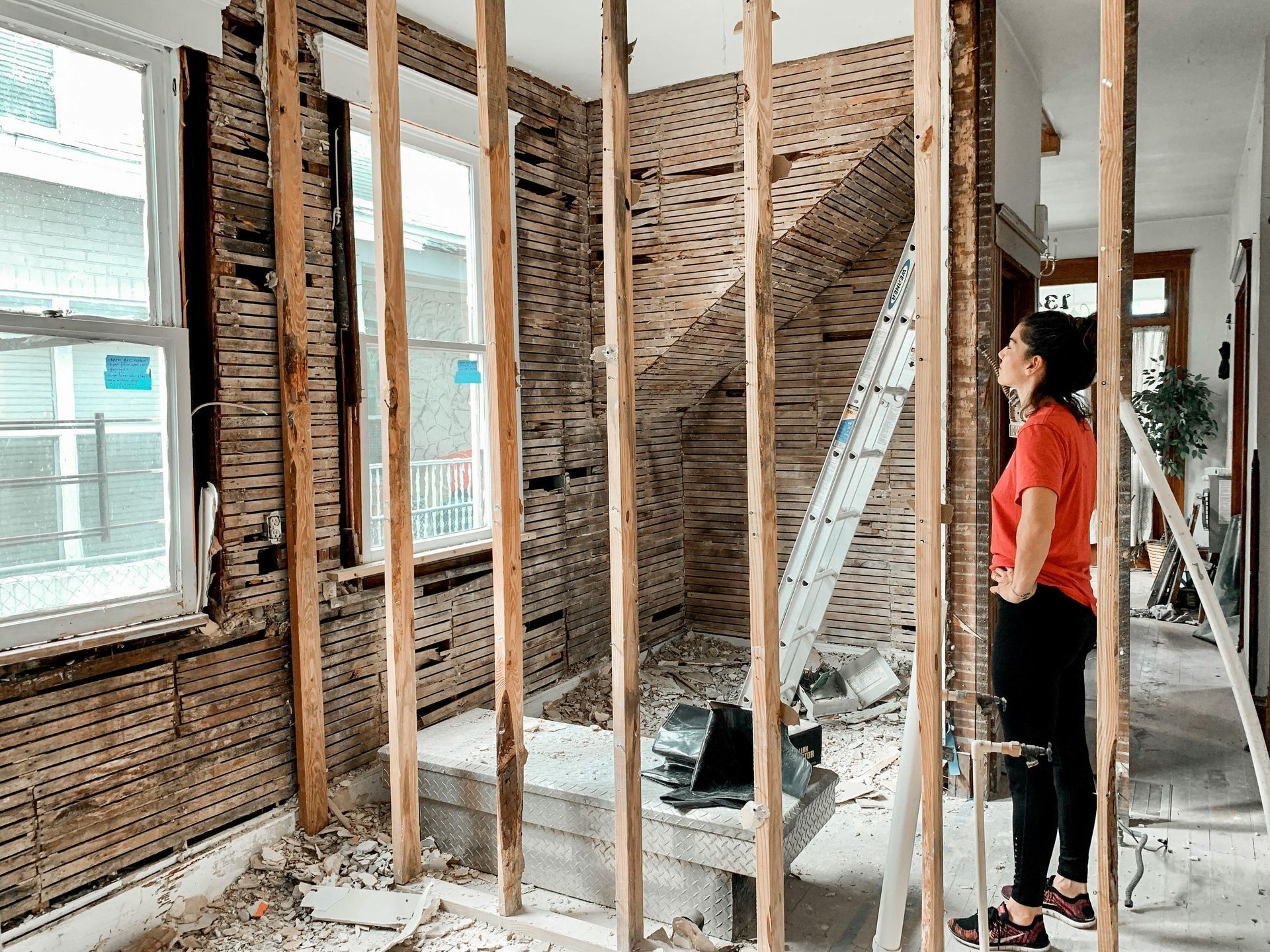 Woman looking at a room under renovation. Walls are stripped to studs, ladder visible.