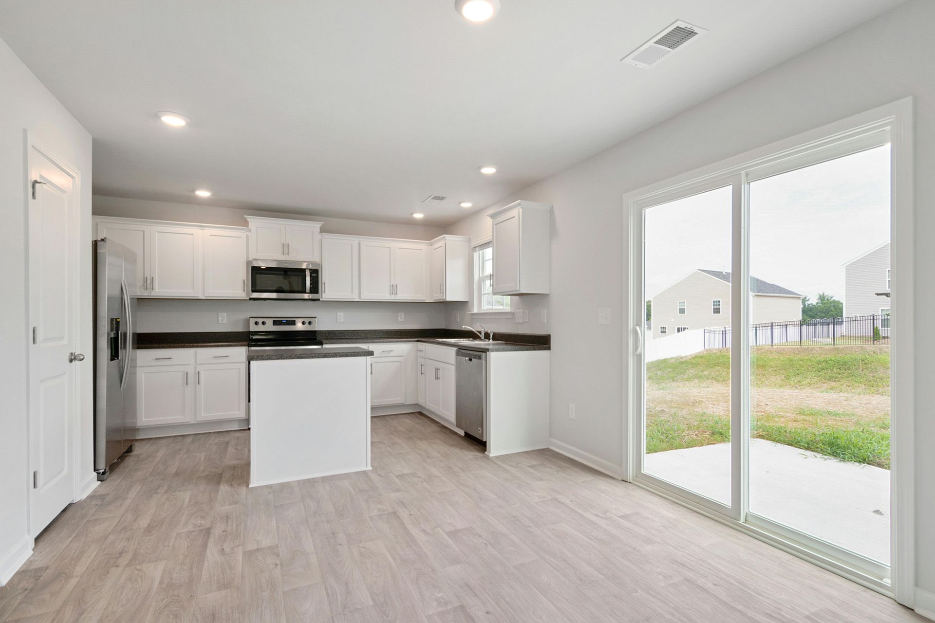 Modern white kitchen with stainless steel appliances, dark countertops, and a sliding glass door to a yard.