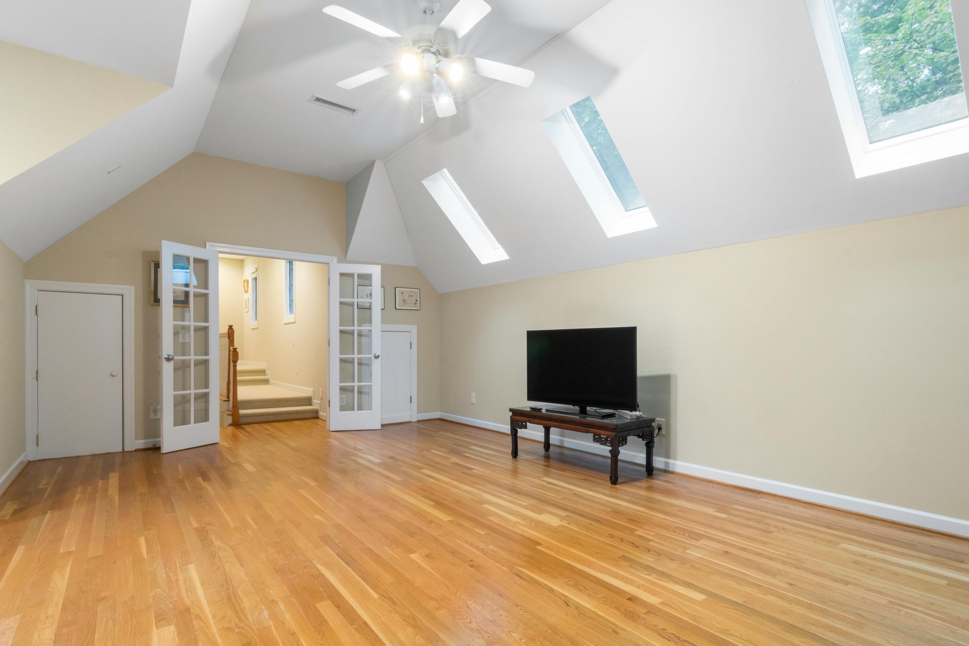 Bright, spacious room with hardwood floors, vaulted ceiling, skylights, and a television on a stand.