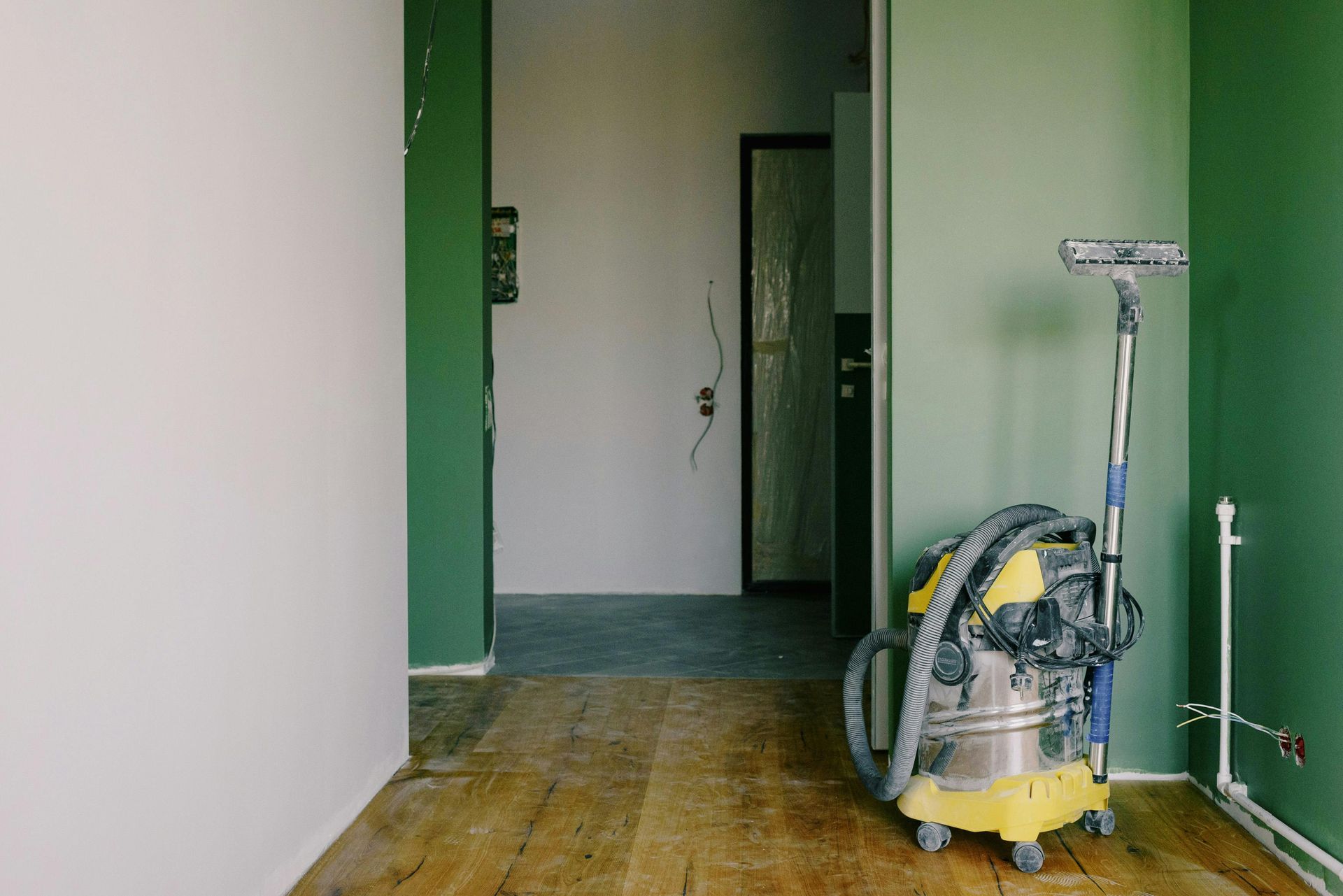 Room under renovation with vacuum and squeegee; walls painted white and green; wooden floor.