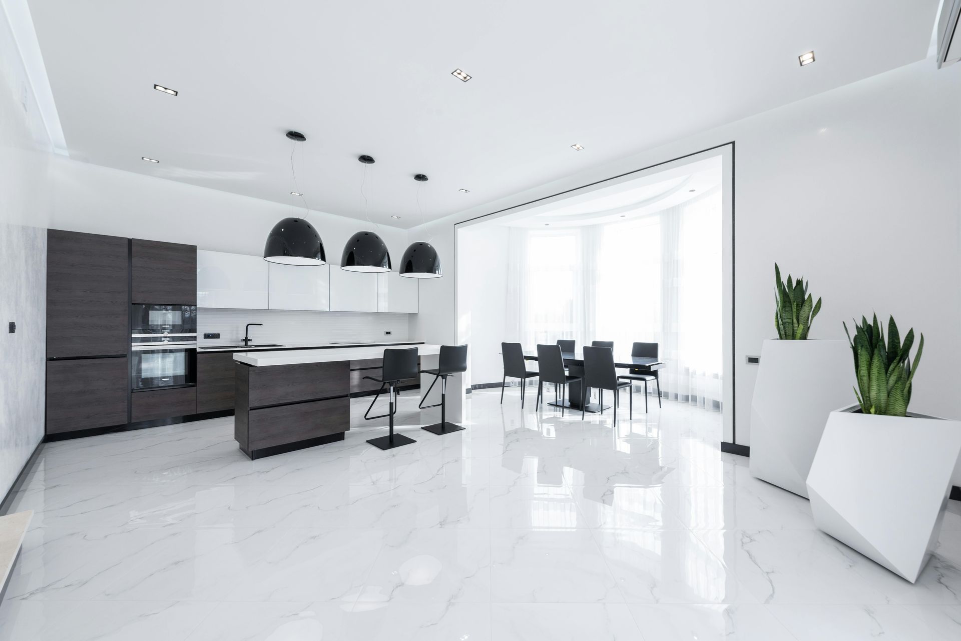 Modern white kitchen with dark wood accents and island, dining table, and large windows.
