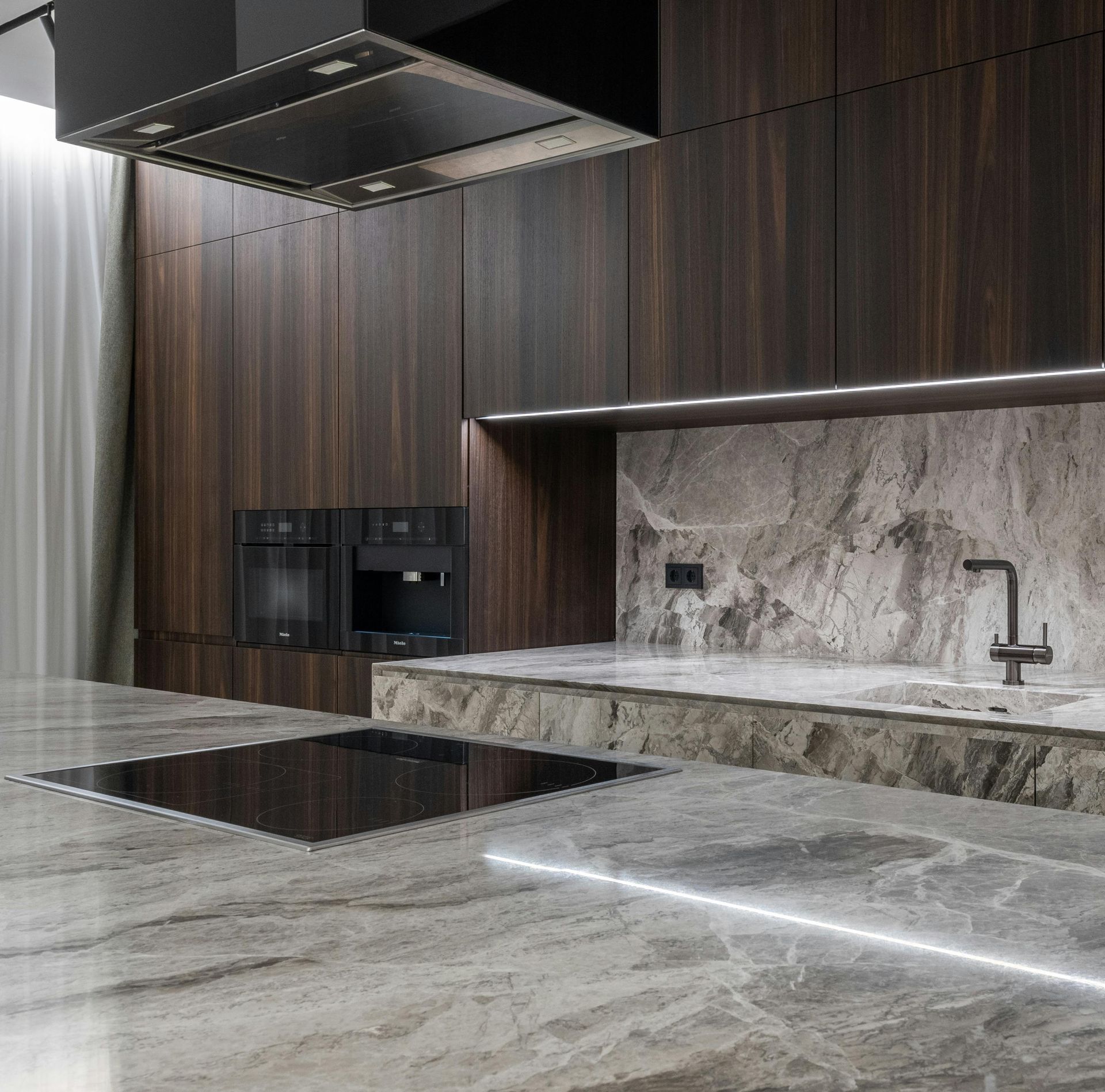 Modern kitchen with dark wood cabinetry, marble countertops, and built-in appliances.