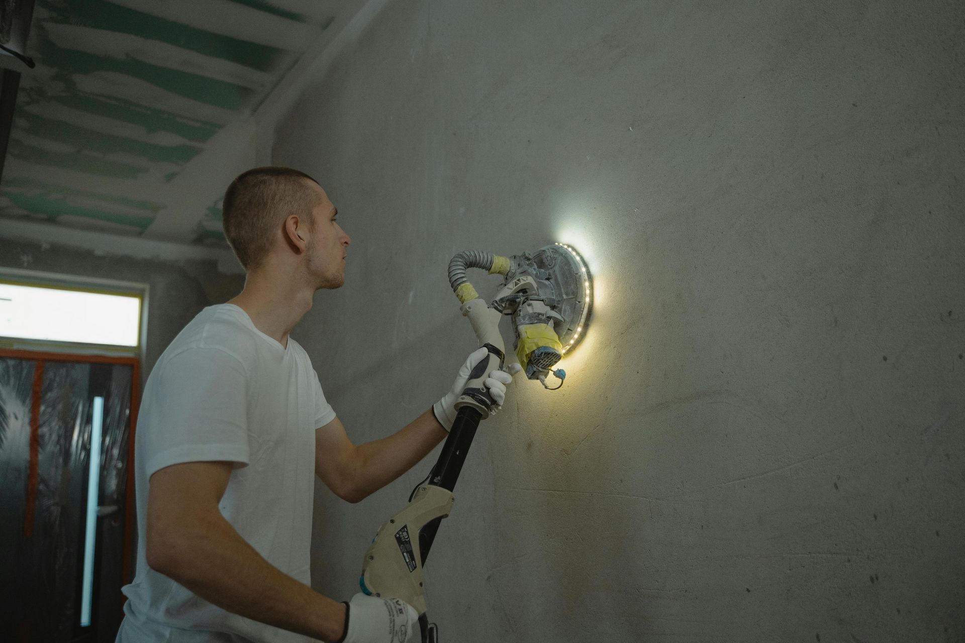 Person sanding a wall with a drywall sander, illuminated by a built-in light.
