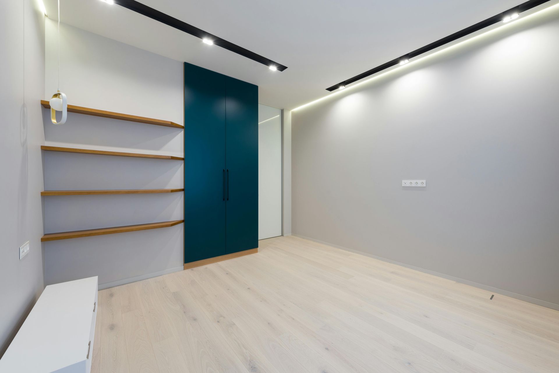 Empty modern room with light wood floors, gray walls, teal closet, and wooden shelves.