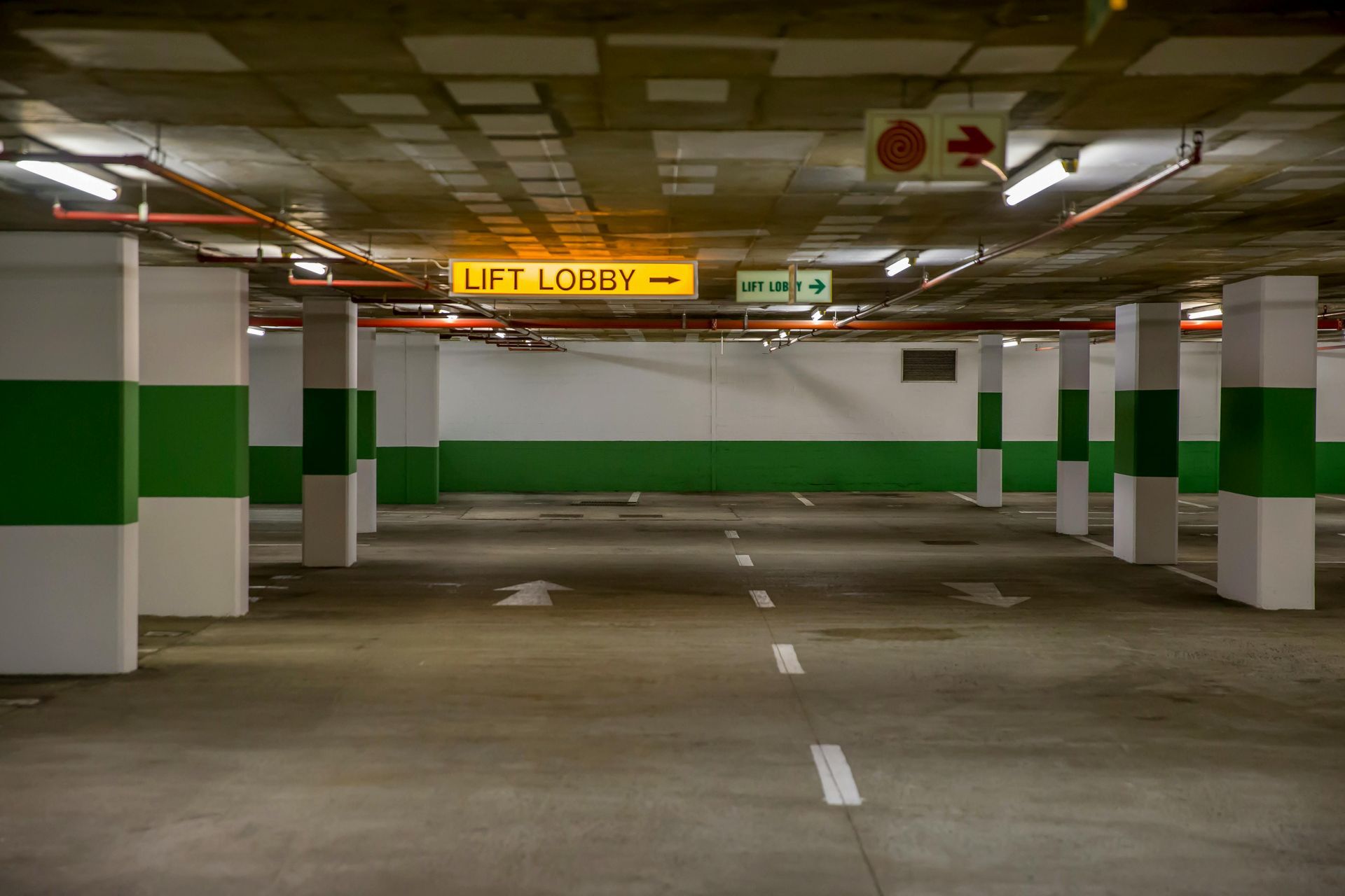 Empty parking garage with white and green columns, directional signs, and overhead lights.