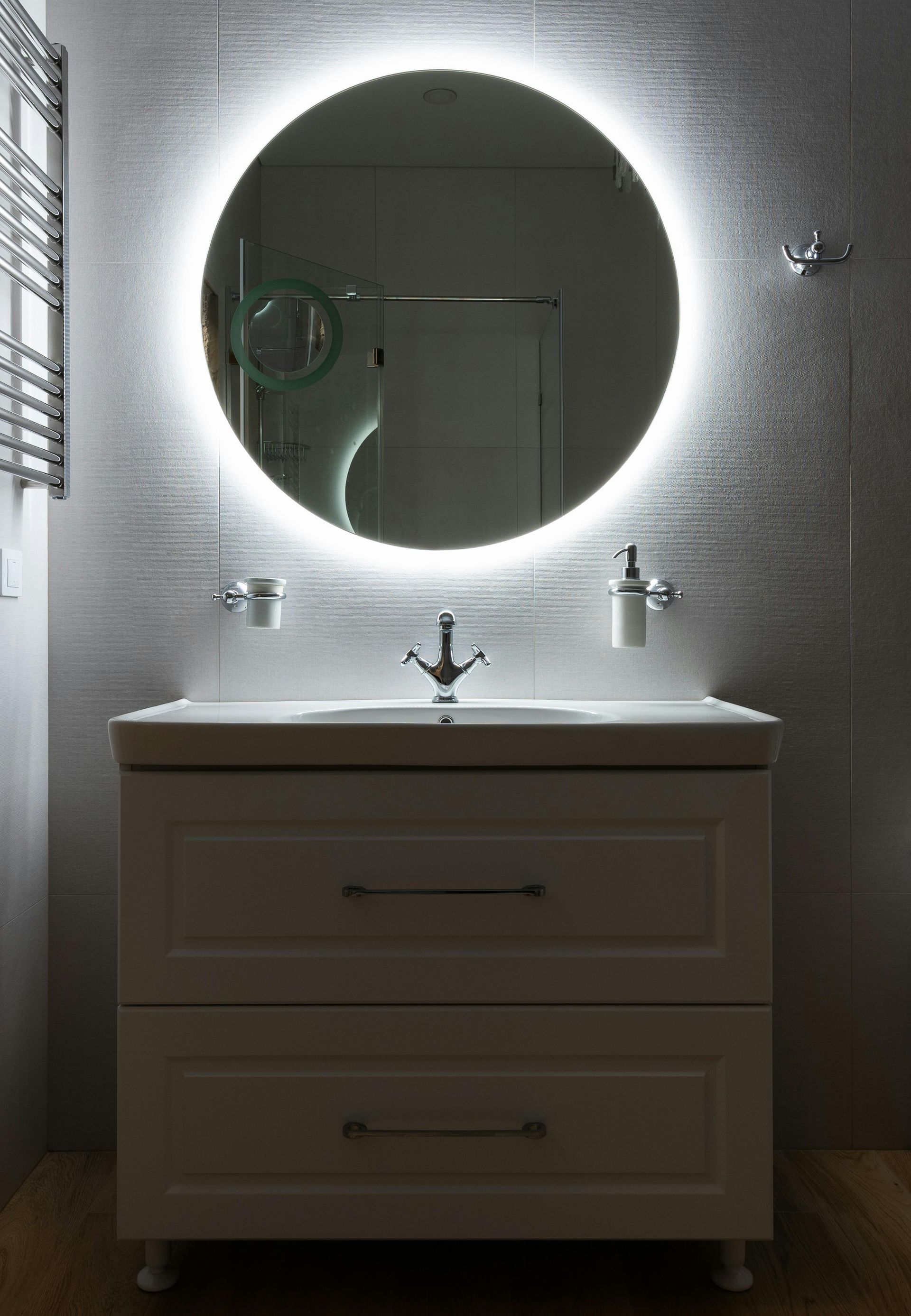 Bathroom vanity with round mirror, LED halo lighting, and a white cabinet.