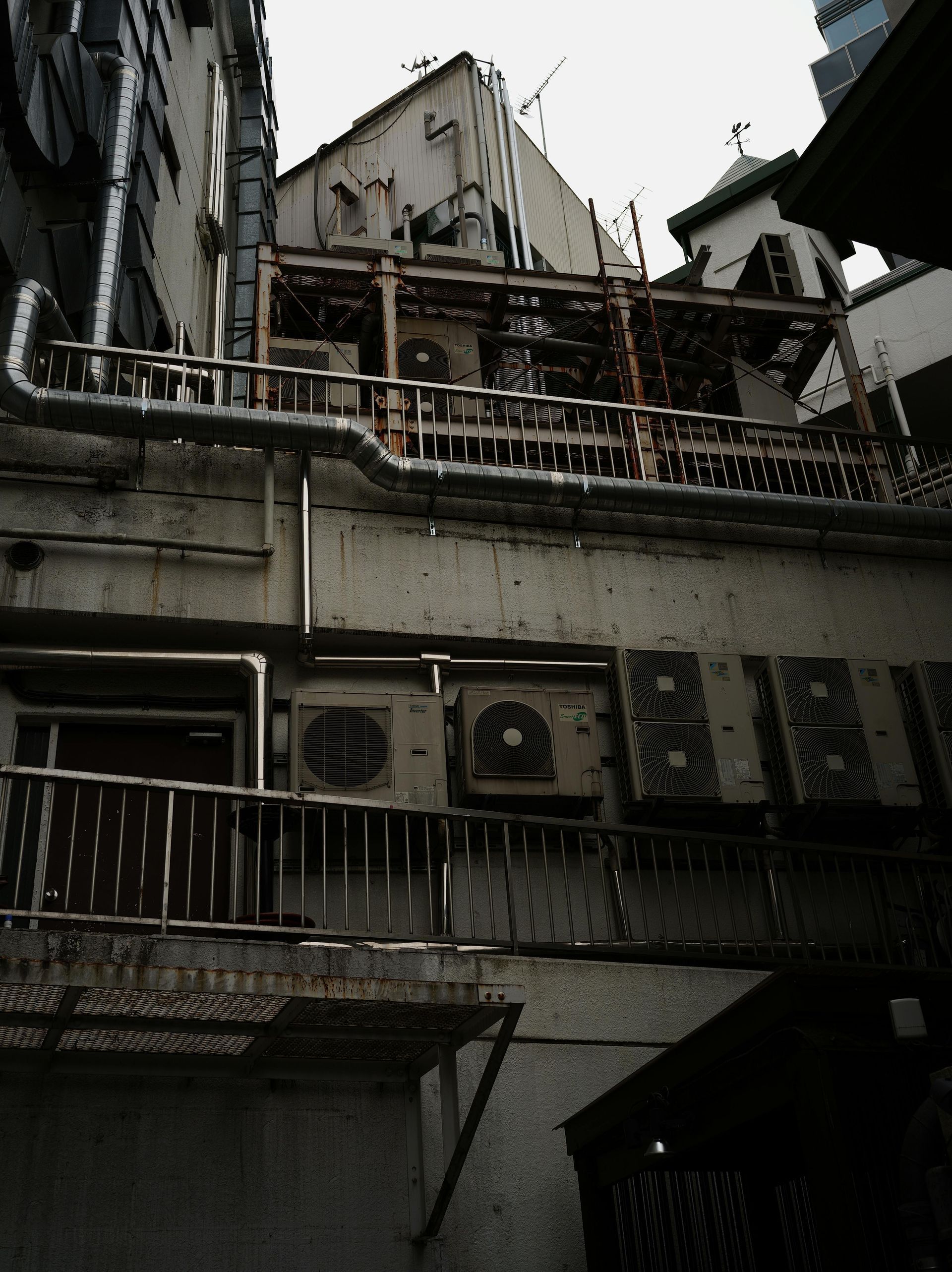 Exterior view of a weathered building with air conditioning units and rusted pipes.