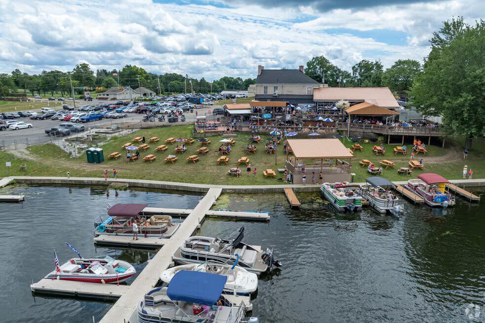 An aerial view of a lakeside restaurant with an outdoor seating area, grassy lawn, and a marina filled with motorboats in Portage Lakes.