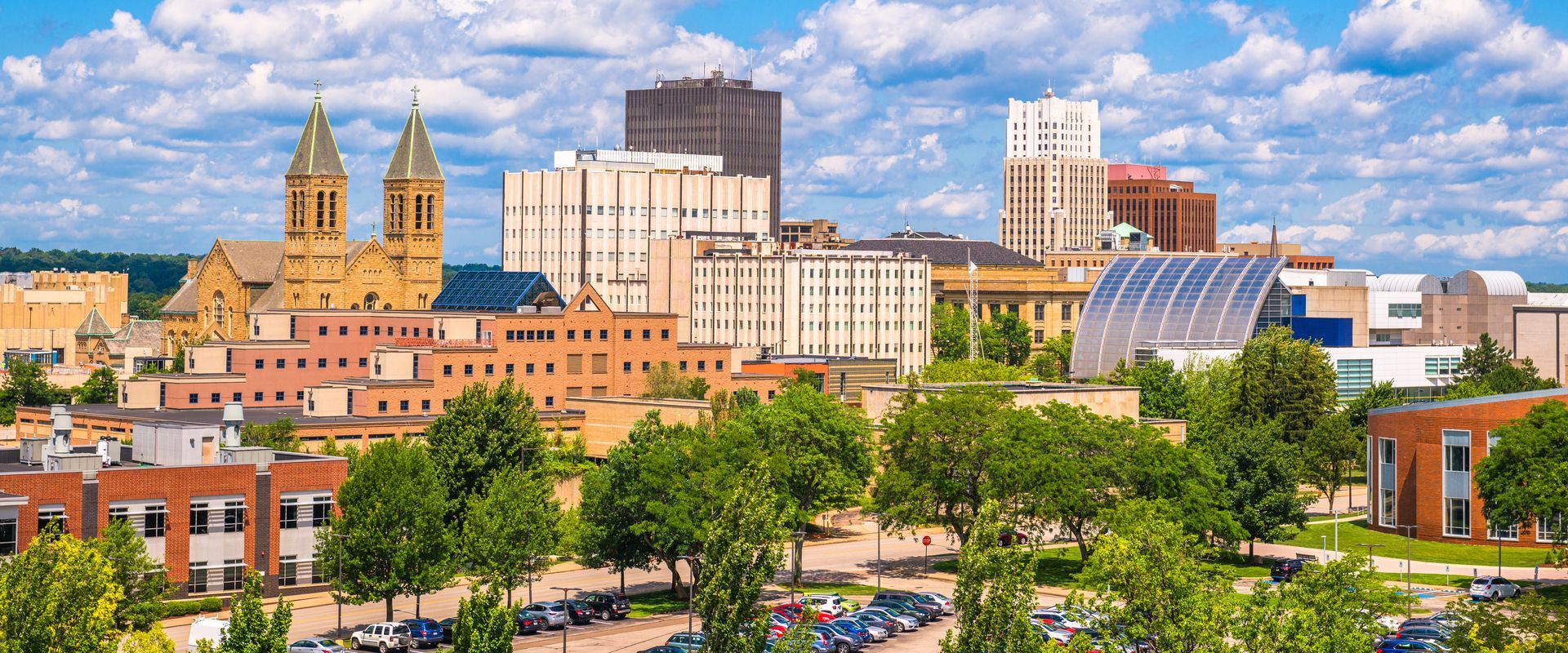 A cityscape of Akron, Ohio, featuring historic brick buildings, a prominent twin-spired church, and a blue sky.