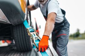 A man is tying a car to a tow truck with a ratchet strap.