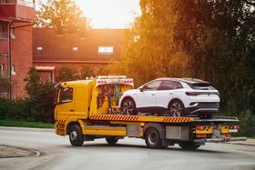 A tow truck is carrying a white car on the back of it.