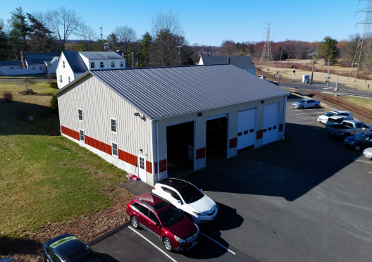 A commercial building with open garage doors; cars in front. White and red exterior with a metal roof. | Bloomfield Garage