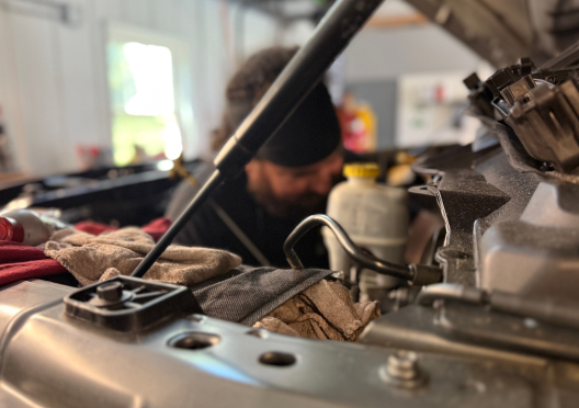 Mechanic working on a car engine under the hood in a garage. | Bloomfield Garage
