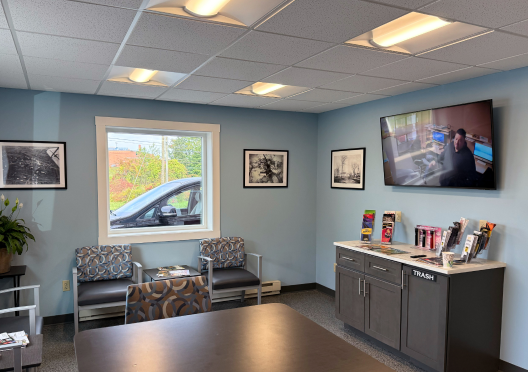 Waiting room with two chairs, window, dark cabinet, TV, and black-and-white art. | Bloomfield Garage