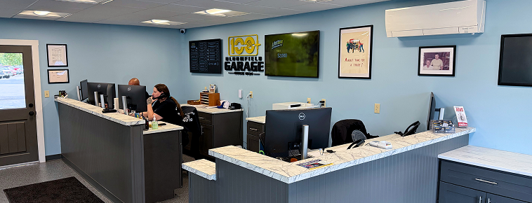 Interior of an office, reception desk with two people at computers, blue walls, a TV, and artwork. | Bloomfield Garage