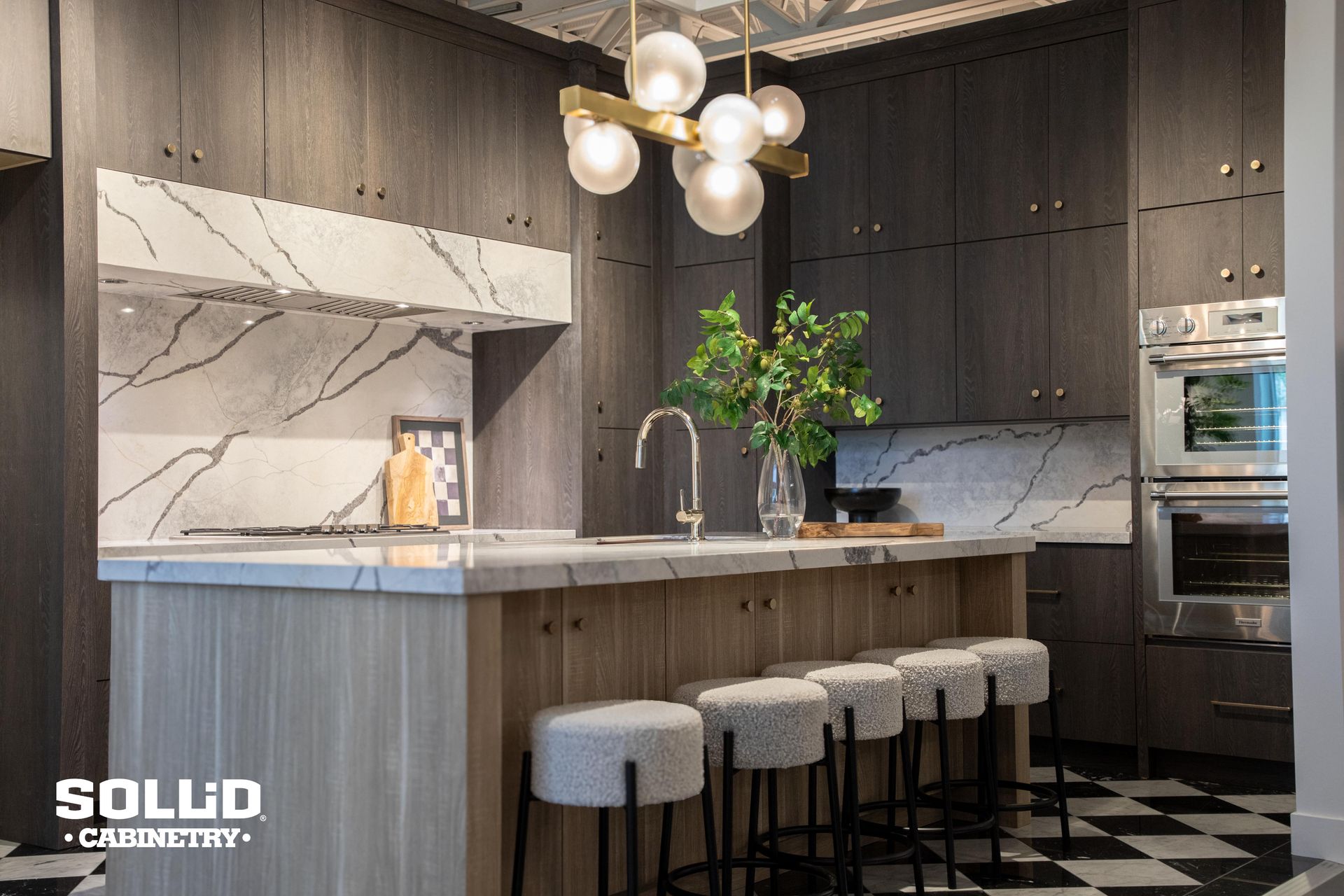 A kitchen with a large island and stools and a checkered floor.