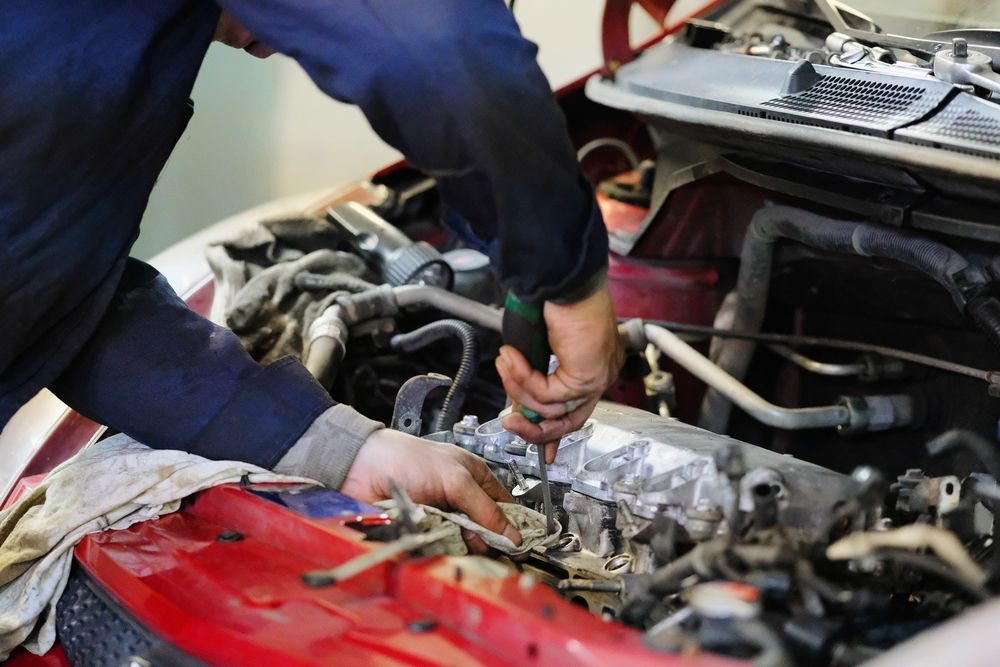 A Mechanic in a Blue Uniform Uses a Screwdriver to Work on a Car Engine — TasMech Auto Services In Mornington, TAS