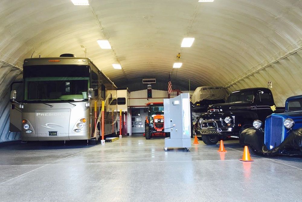 A RV is parked in a garage with other cars