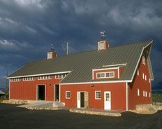A large red barn with a green roof is sitting on top of a dirt field.