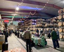 A large warehouse filled with lots of barrels and people standing around tables.