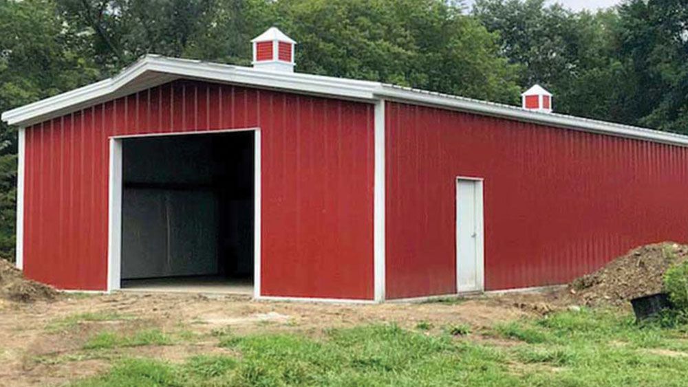 A large red barn with a white roof is sitting in the middle of a grassy field.