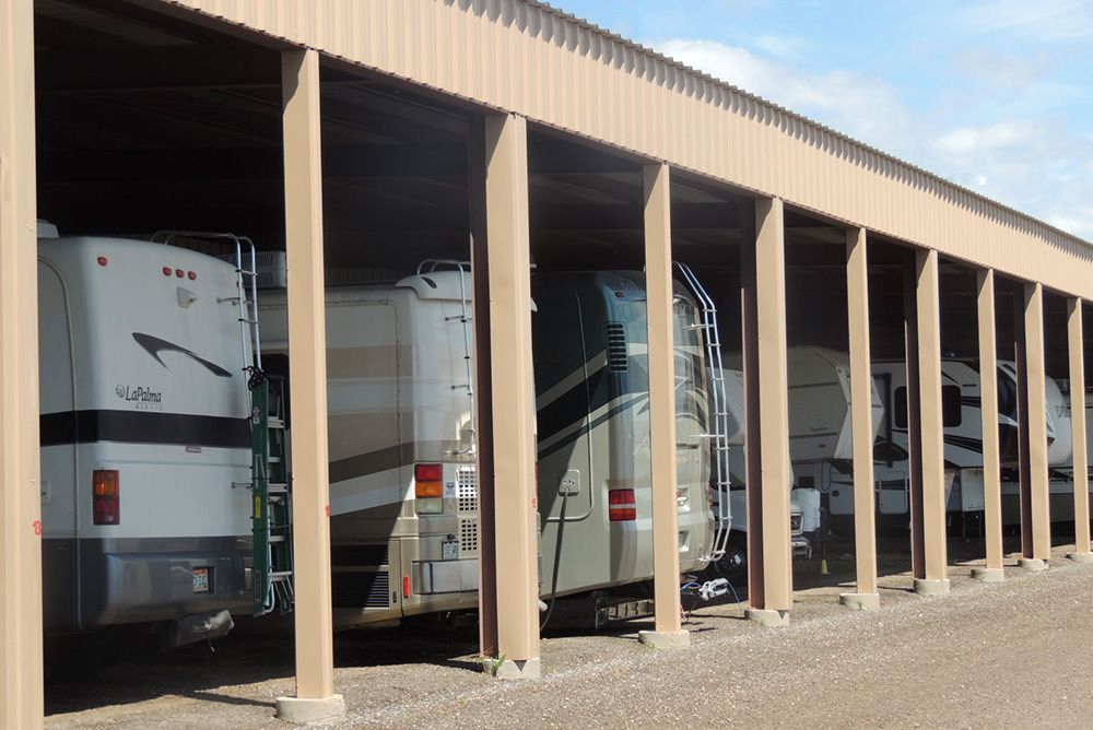 A row of rvs are parked under a shed.