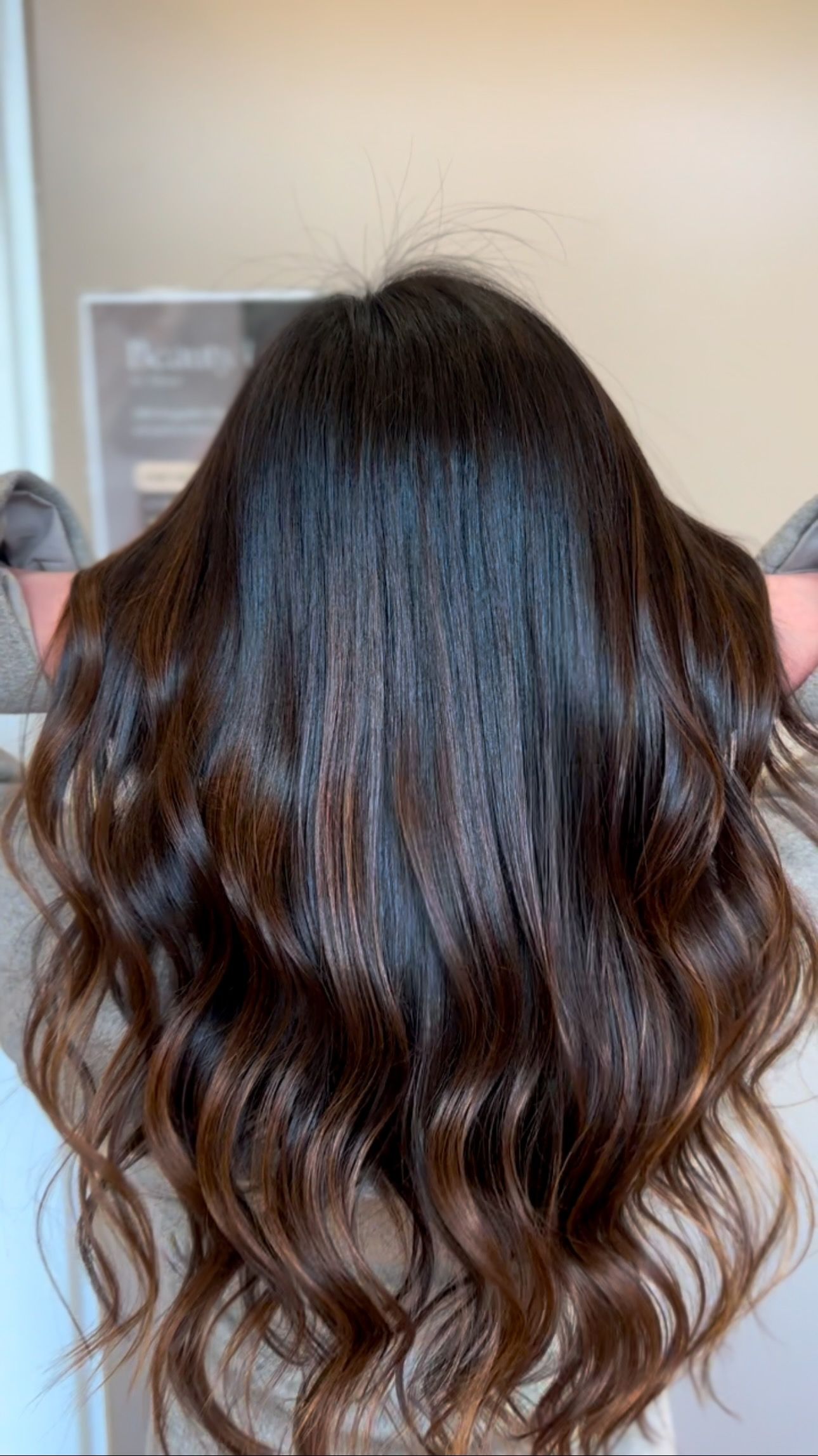 Dark brown hair with ombre effect, wavy, held up in front, against a wall.