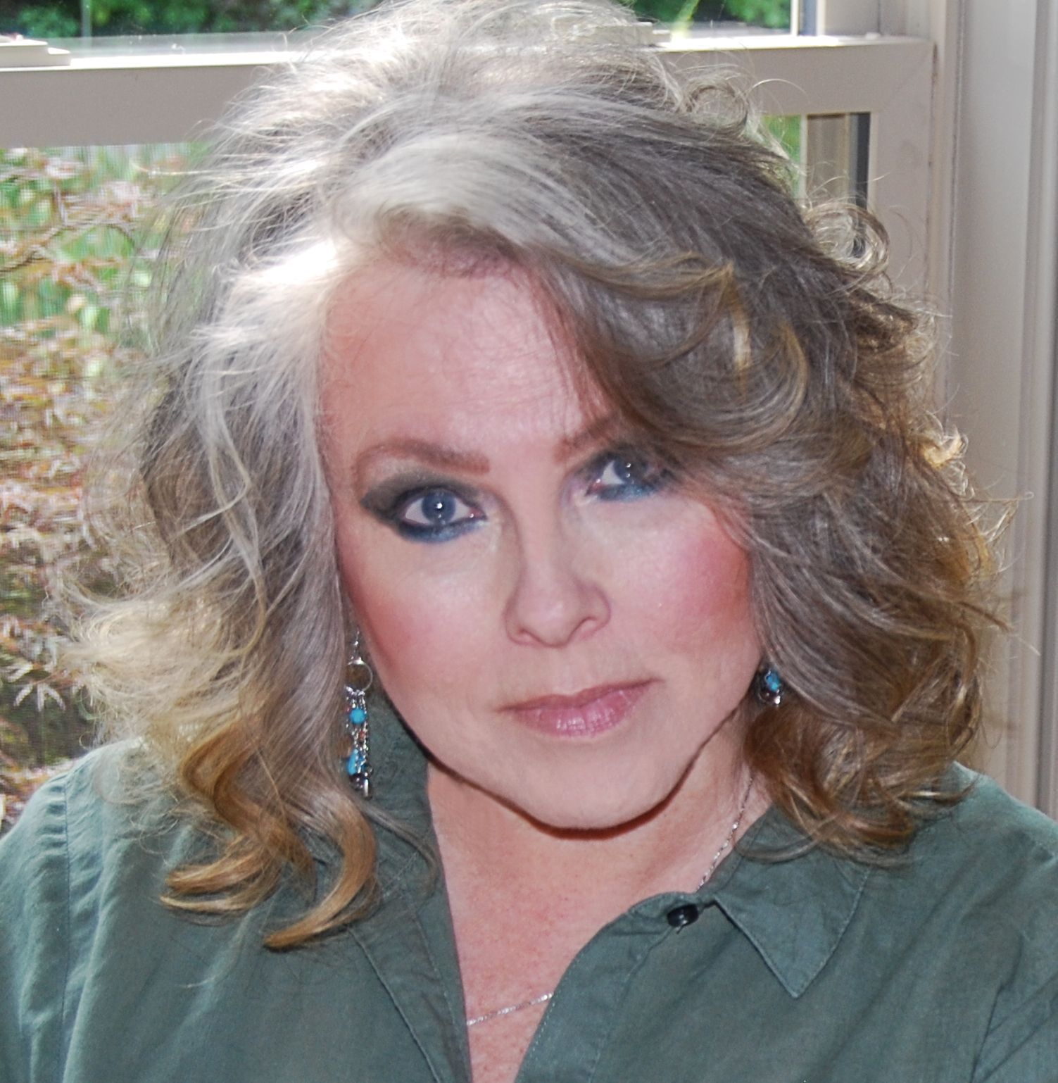 A woman with gray hair is wearing a green shirt and earrings