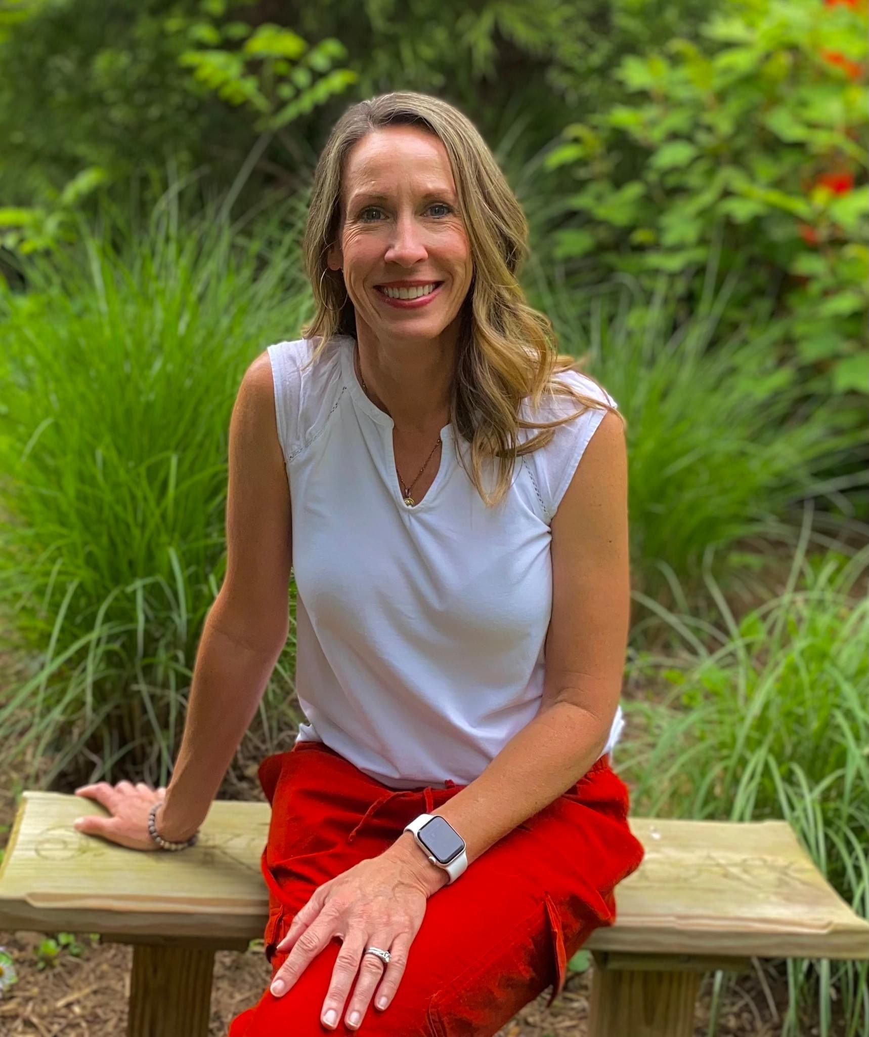 A woman in a white shirt and red pants is sitting on a wooden bench.