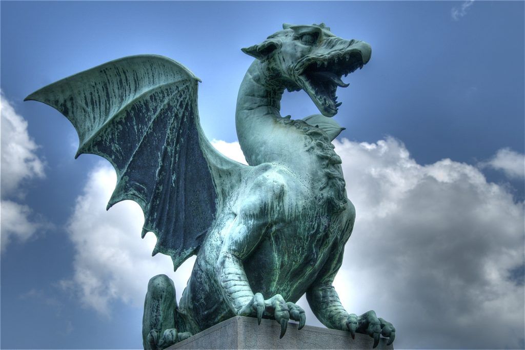 A statue of a dragon with wings is sitting on a rock.