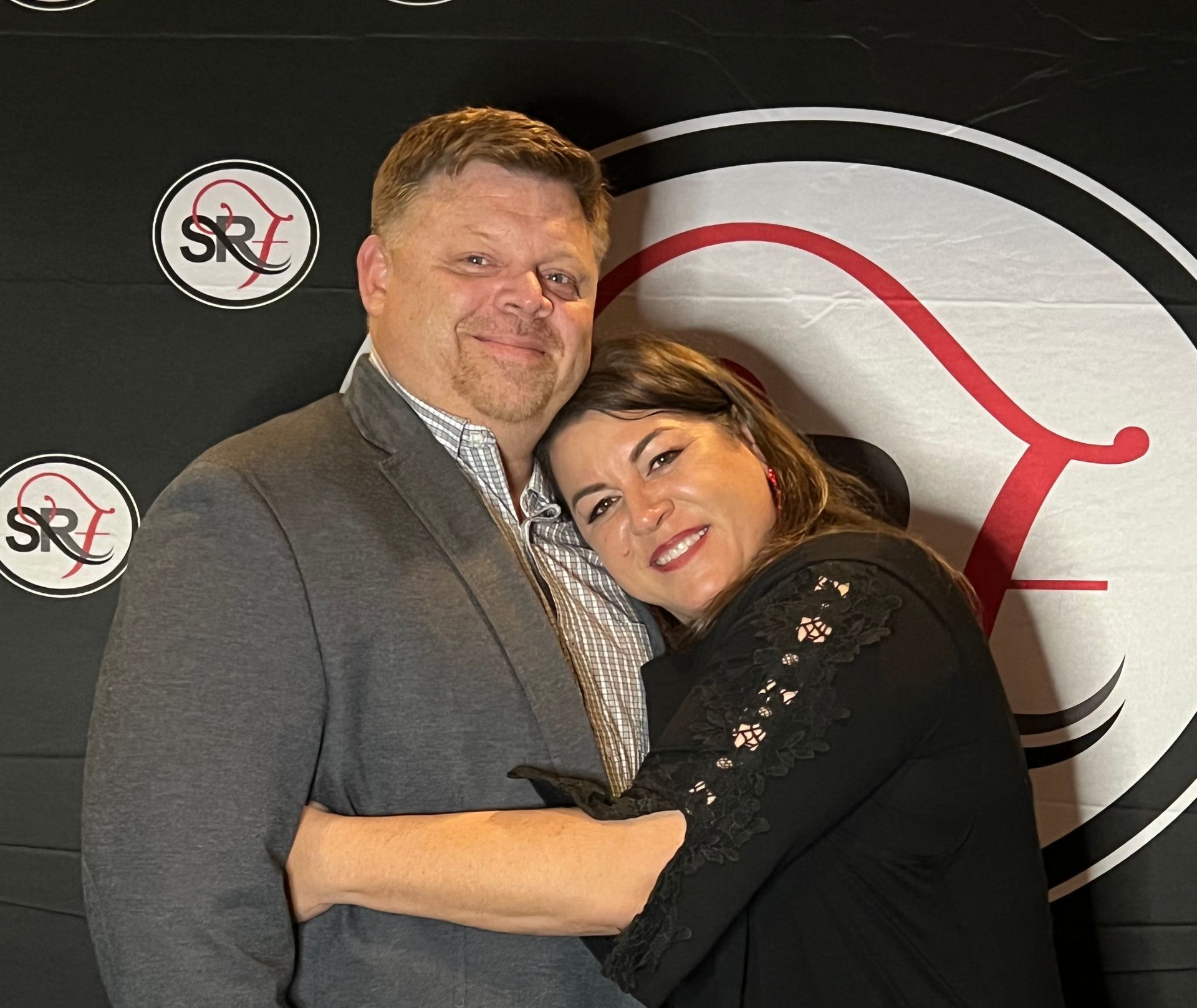 A man and woman are posing for a picture in front of a sr logo