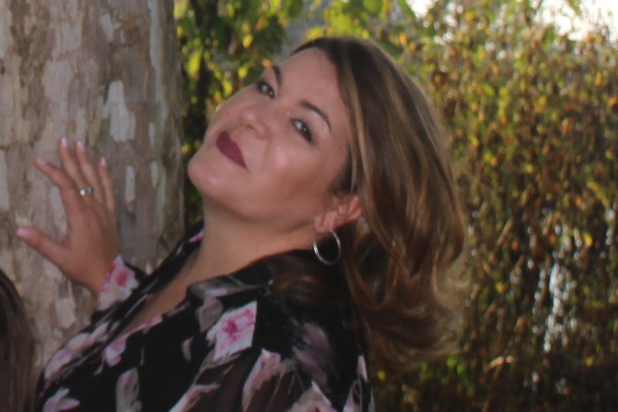 A woman in a floral shirt is leaning against a tree.