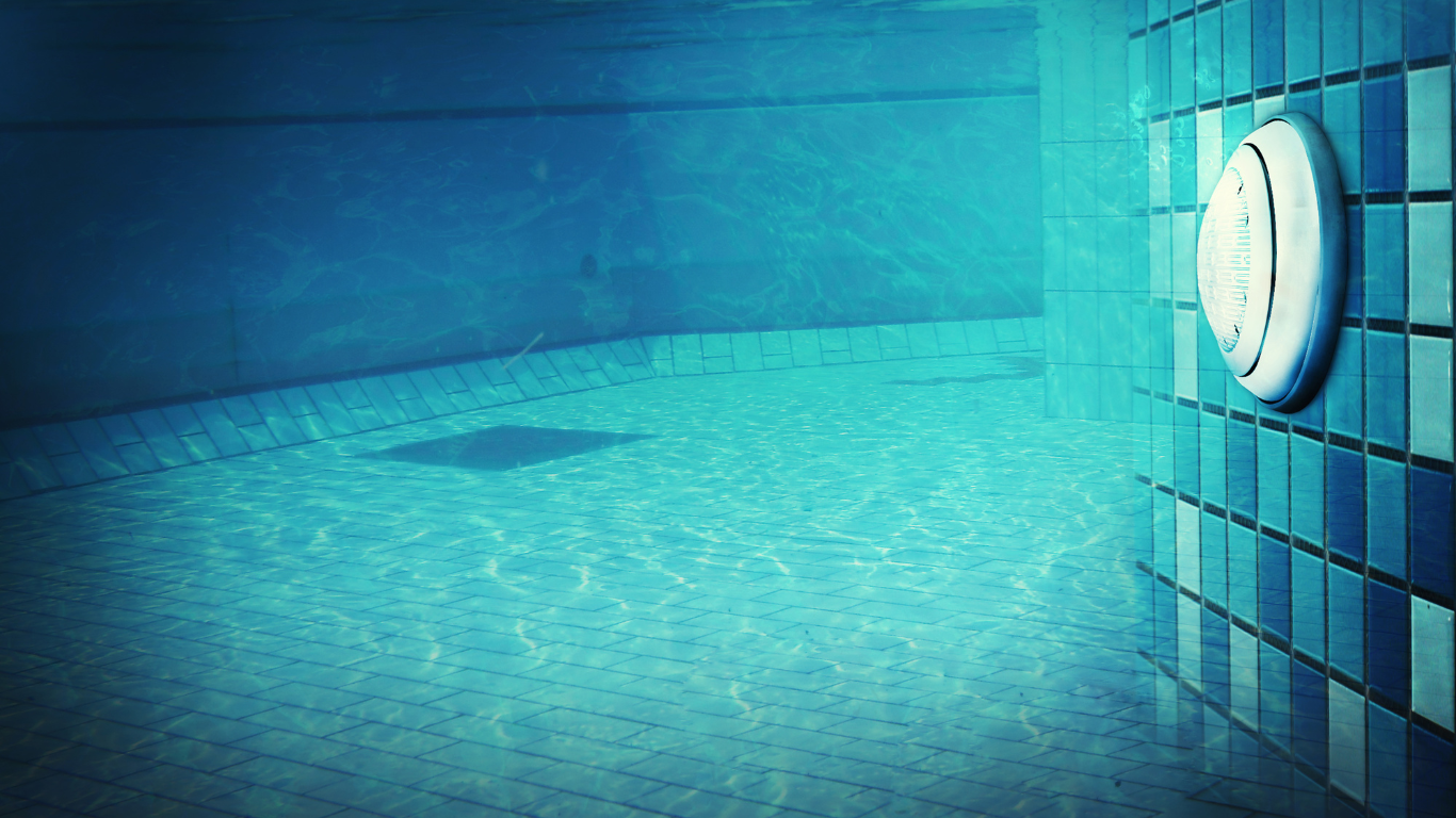 Blue-tiled swimming pool wall with a round clock and rippled water reflections