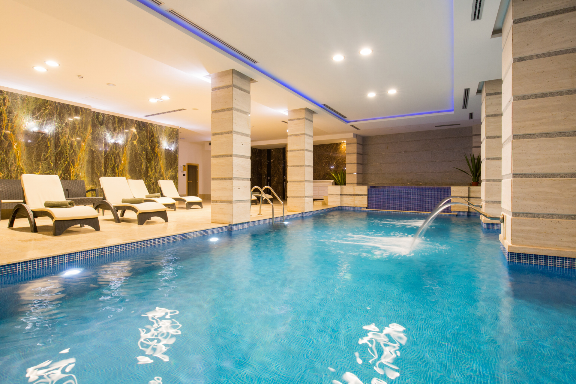 Indoor hotel pool with lounge chairs, warm lighting, and blue water