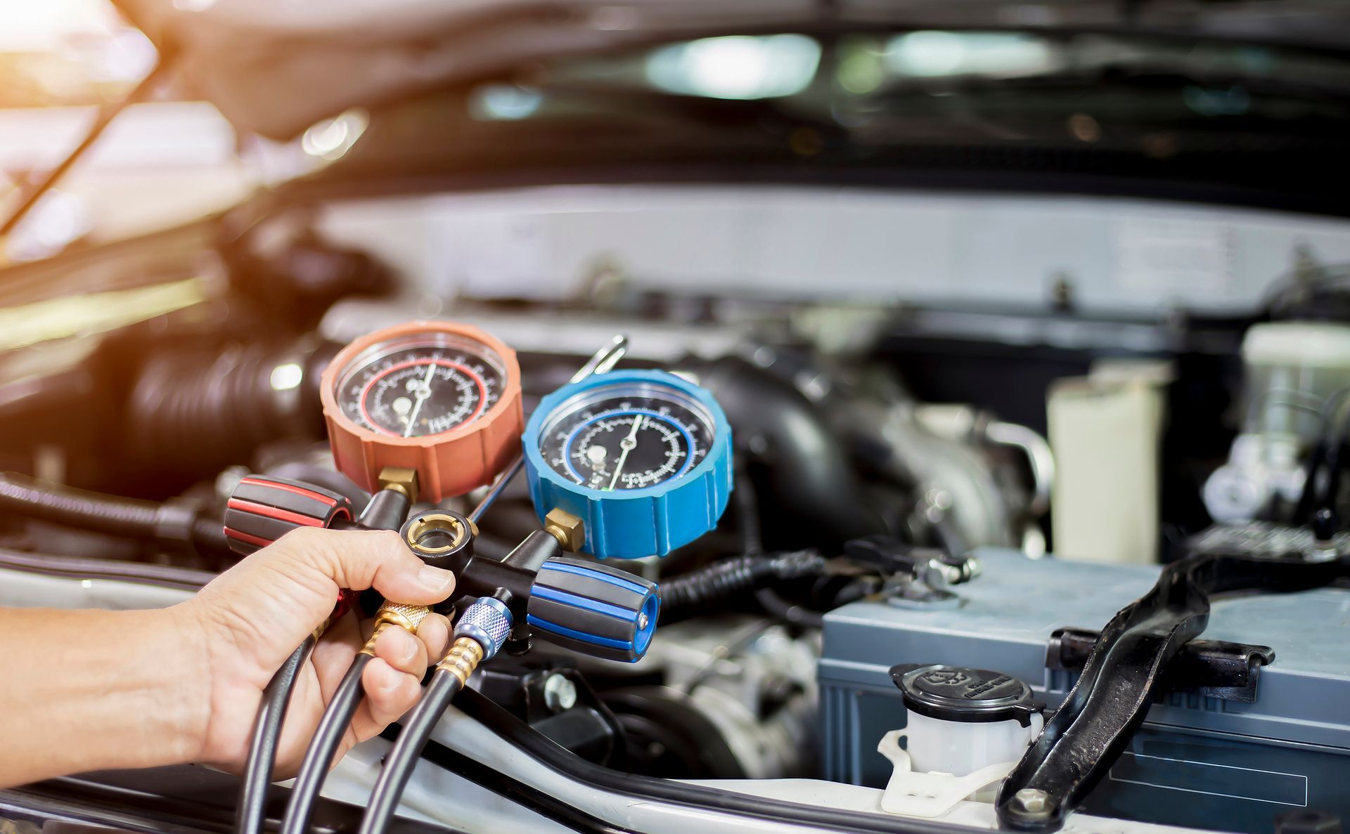 Hand holding gauges, checking car's AC system in an engine bay. Gauges are red and blue.