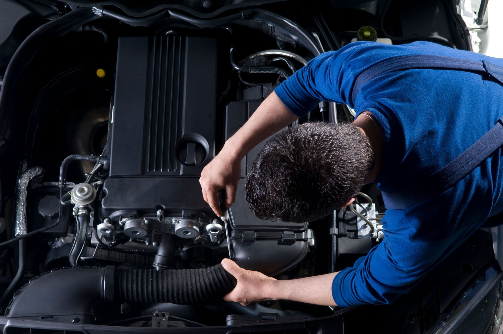 Mechanic working on a car engine; wearing blue uniform, hands at work.