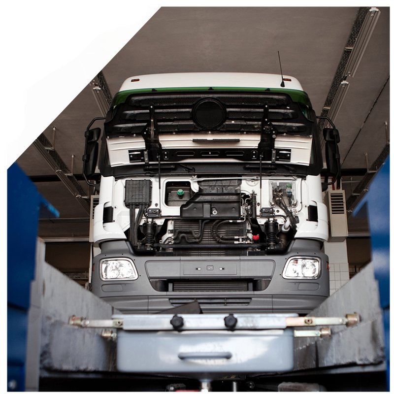 White truck undergoing repair in a maintenance bay, front view.