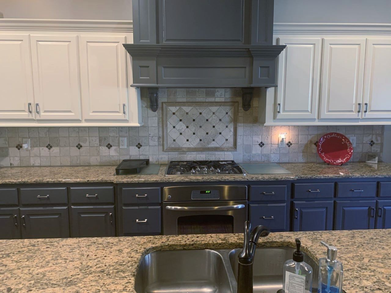A kitchen with gray cabinets , white cabinets , stainless steel appliances , granite counter tops and a sink.