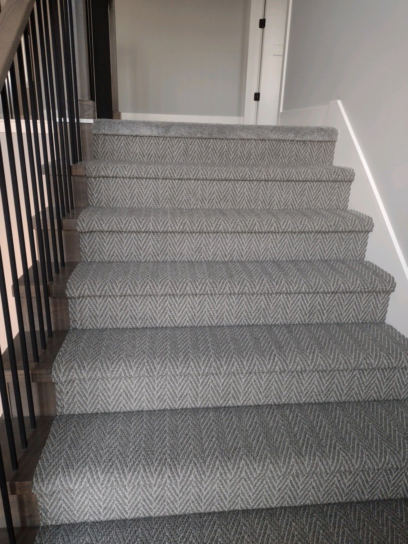 A set of stairs with a gray carpet and a metal railing.