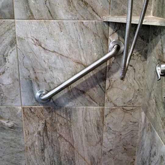 A shower with a stainless steel hand rail and a shower head.