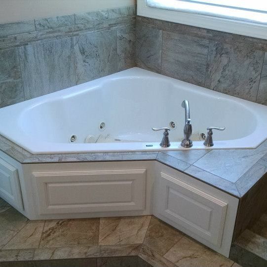 A corner bathtub in a bathroom next to a window