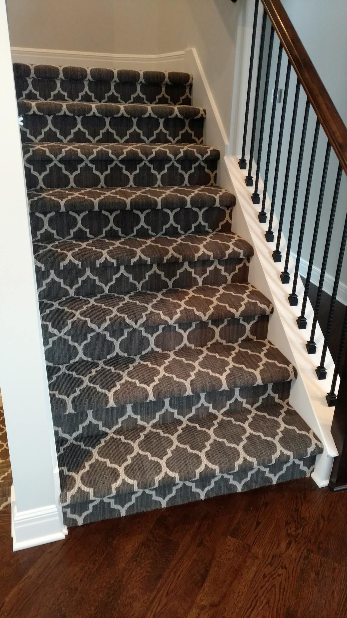 A staircase with a carpet on the steps and a wrought iron railing.