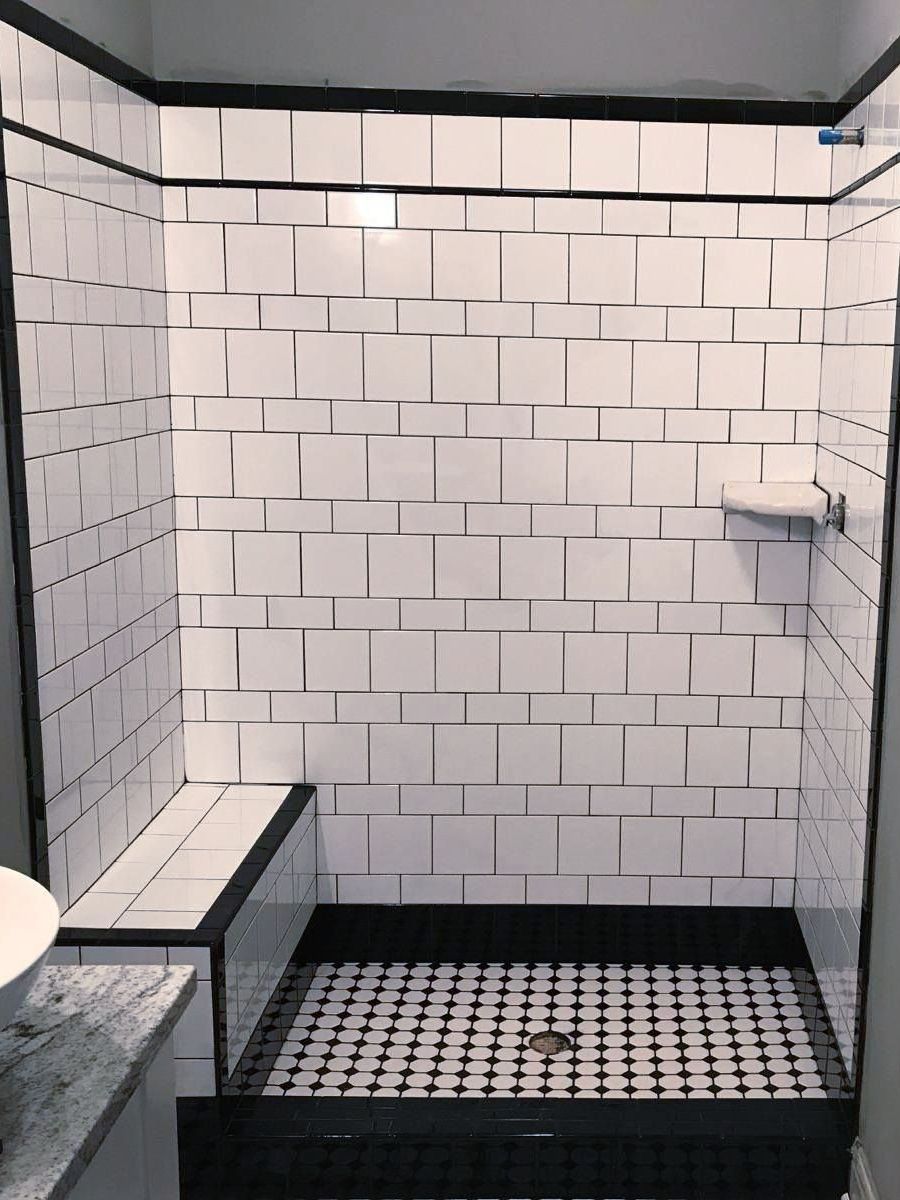A bathroom with white tiles and a black and white mosaic floor