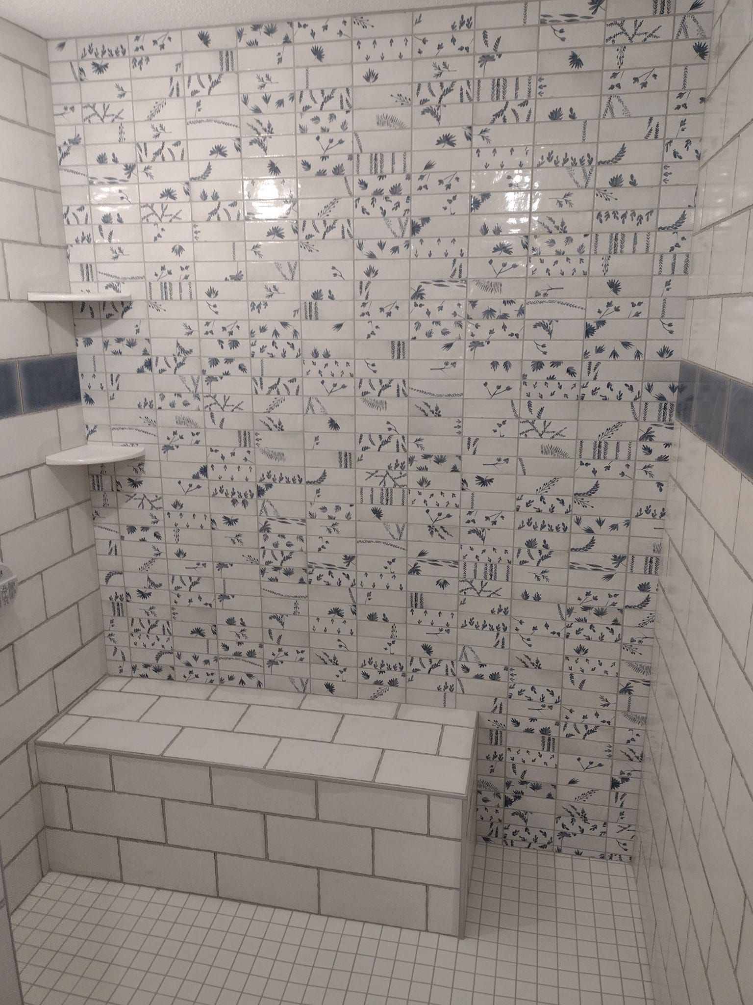 A bathroom with white tiles and a bench in the shower.
