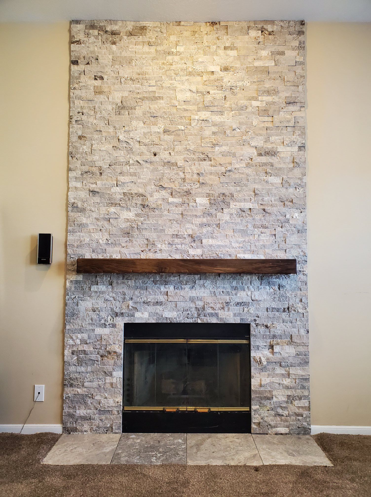 A fireplace with a stone wall and a wooden mantle in a living room.